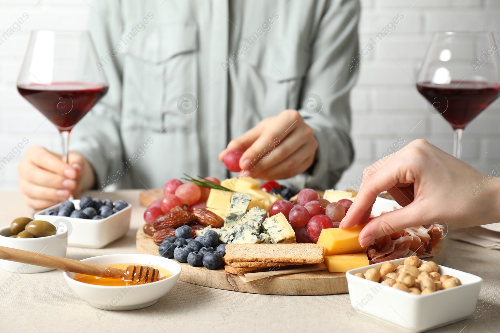 Photo of Women enjoying different snacks and wine during brunch at light grey table indoors, closeup