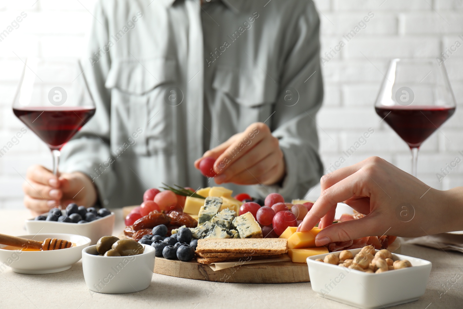 Photo of Women enjoying different snacks and wine during brunch at light grey table indoors, closeup