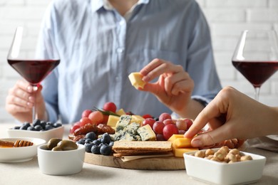 Photo of Women enjoying different snacks and wine during brunch at light grey table indoors, closeup