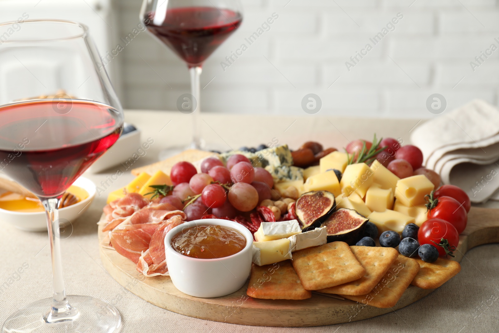 Photo of Different types of delicious cheese, other snacks and wine on light grey table, closeup