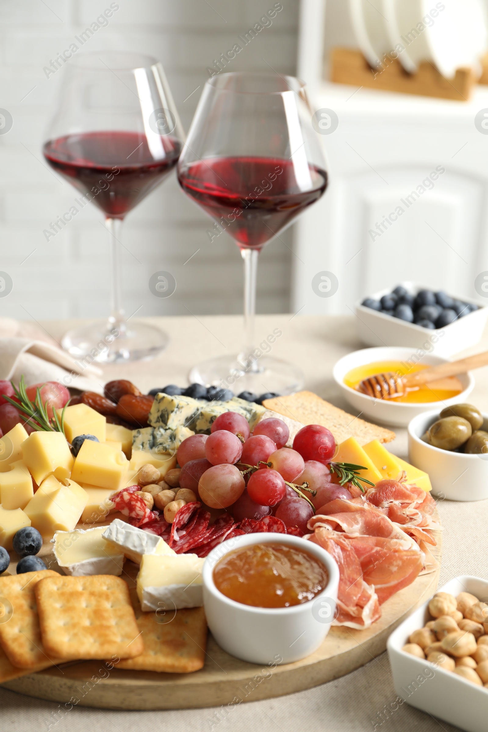 Photo of Different types of delicious cheese, other snacks and wine on light grey table, closeup