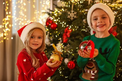 Photo of Little kids in Santa hats with Christmas ornaments at home