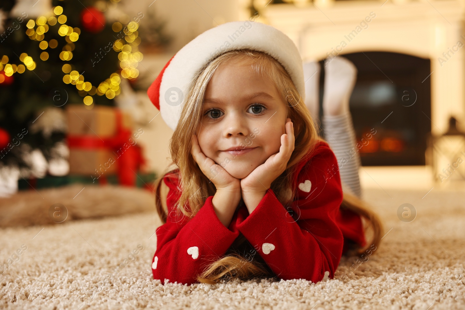 Photo of Little girl in Santa hat on floor at home. Christmas celebration