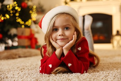 Photo of Little girl in Santa hat on floor at home. Christmas celebration