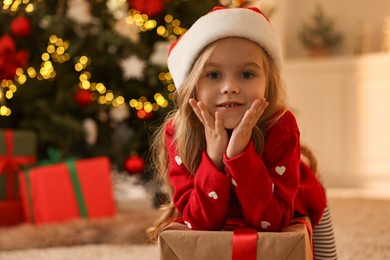 Photo of Little girl in Santa hat with Christmas box at home, space for text