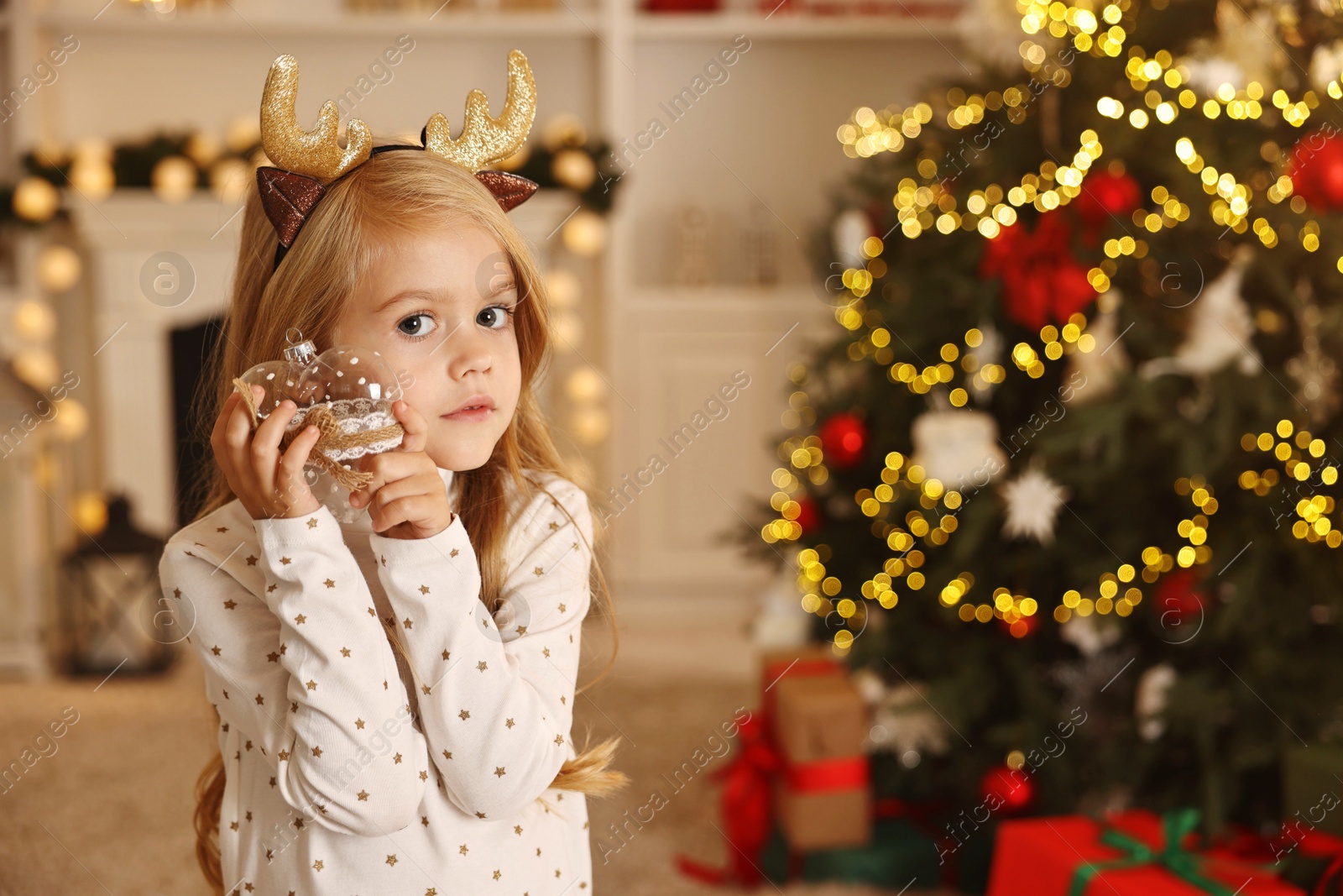 Photo of Little girl with Christmas ornament at home, space for text