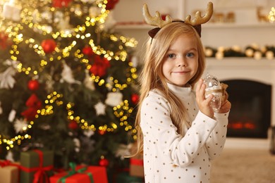 Photo of Little girl with Christmas ornament at home, space for text