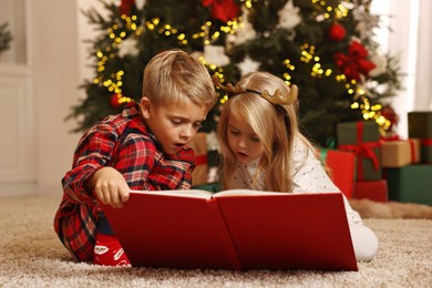 Photo of Little kids reading book on floor at home. Christmas celebration