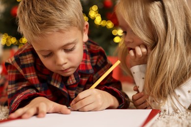 Photo of Little kids writing letter to Santa Claus on floor at home. Christmas celebration