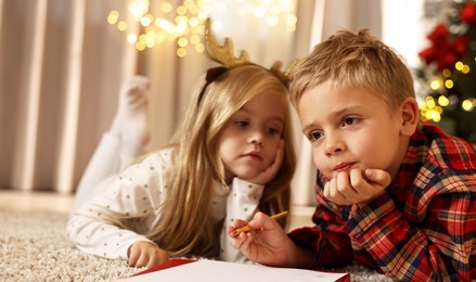 Photo of Little kids writing letter to Santa Claus on floor at home. Christmas celebration