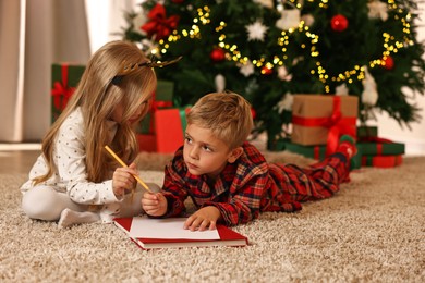 Photo of Little kids writing letter to Santa Claus on floor at home. Christmas celebration