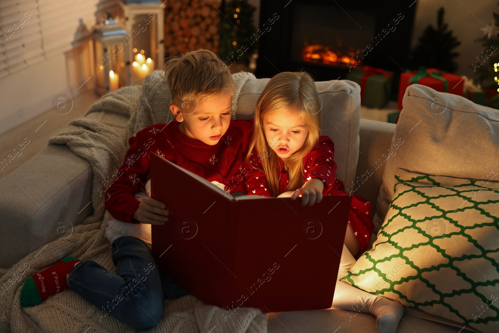 Photo of Little kids reading book on sofa at home. Christmas celebration