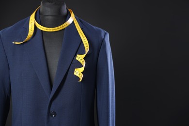 Photo of Male mannequin with jacket and measuring tape on dark background, closeup. Space for text