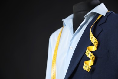 Photo of Male mannequin with jacket, shirt and measuring tape on black background, closeup. Space for text