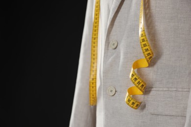 Photo of Male mannequin with jacket and measuring tape on black background, closeup. Space for text