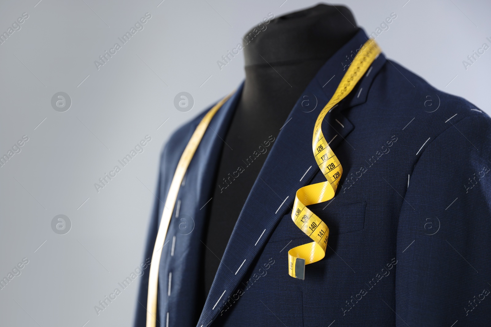 Photo of Semi-ready jacket and measuring tape on mannequin against gray background, closeup. Space for text