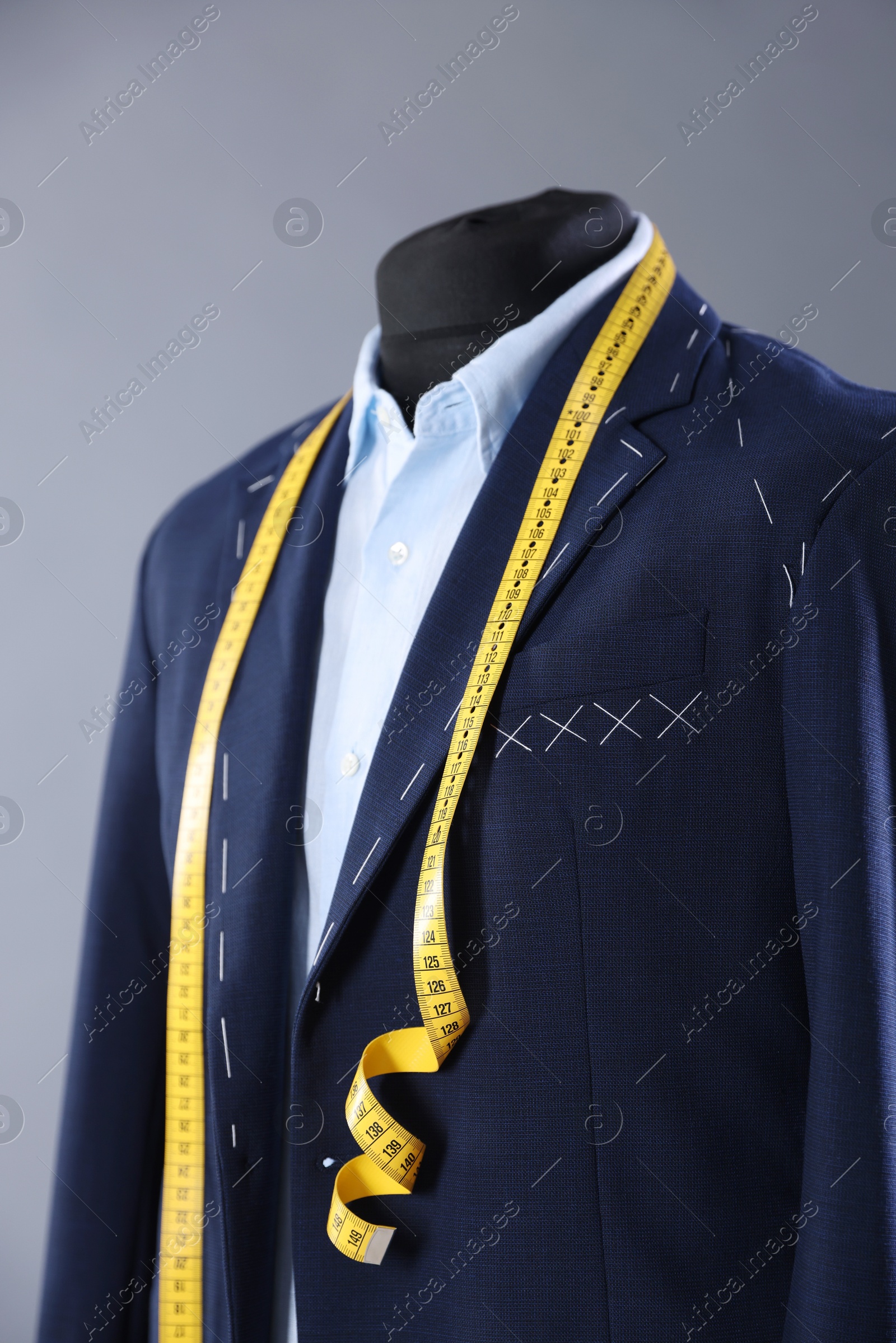 Photo of Semi-ready jacket, shirt and measuring tape on mannequin against gray background, closeup