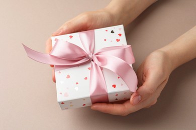 Photo of Woman holding gift box with pink bow on beige background, closeup