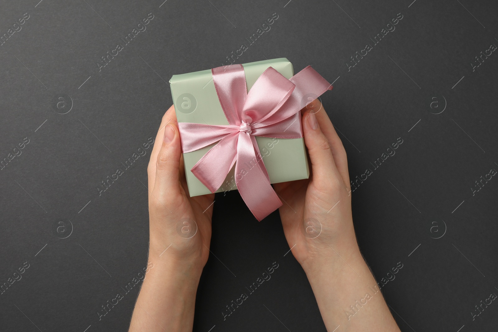 Photo of Woman holding gift box with pink bow on black background, top view