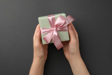 Photo of Woman holding gift box with pink bow on black background, top view