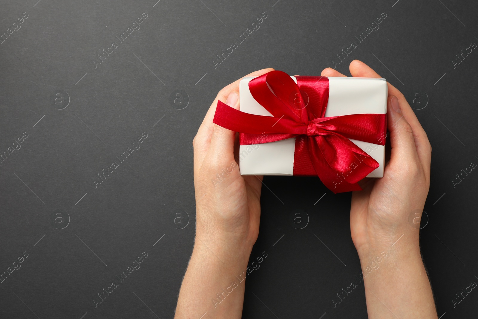 Photo of Woman holding gift box with red bow on black background, top view. Space for text