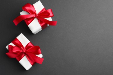 Photo of Gift boxes with red bows on black background, top view. Space for text