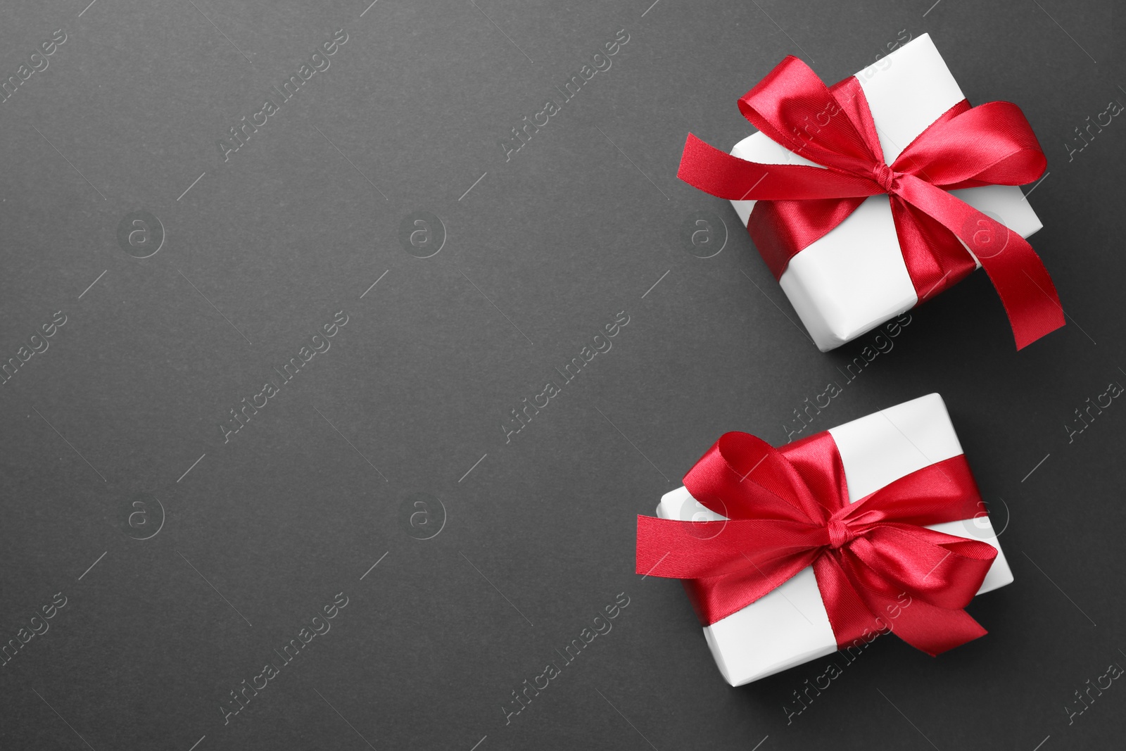 Photo of Gift boxes with red bows on black background, top view. Space for text