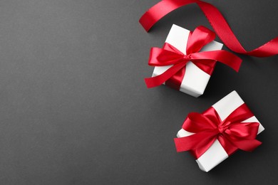 Photo of Gift boxes with red bows and ribbon on black background, top view. Space for text