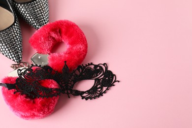 Photo of Fluffy handcuffs, lace mask and high-heeled shoes on pink background, flat lay. Space for text