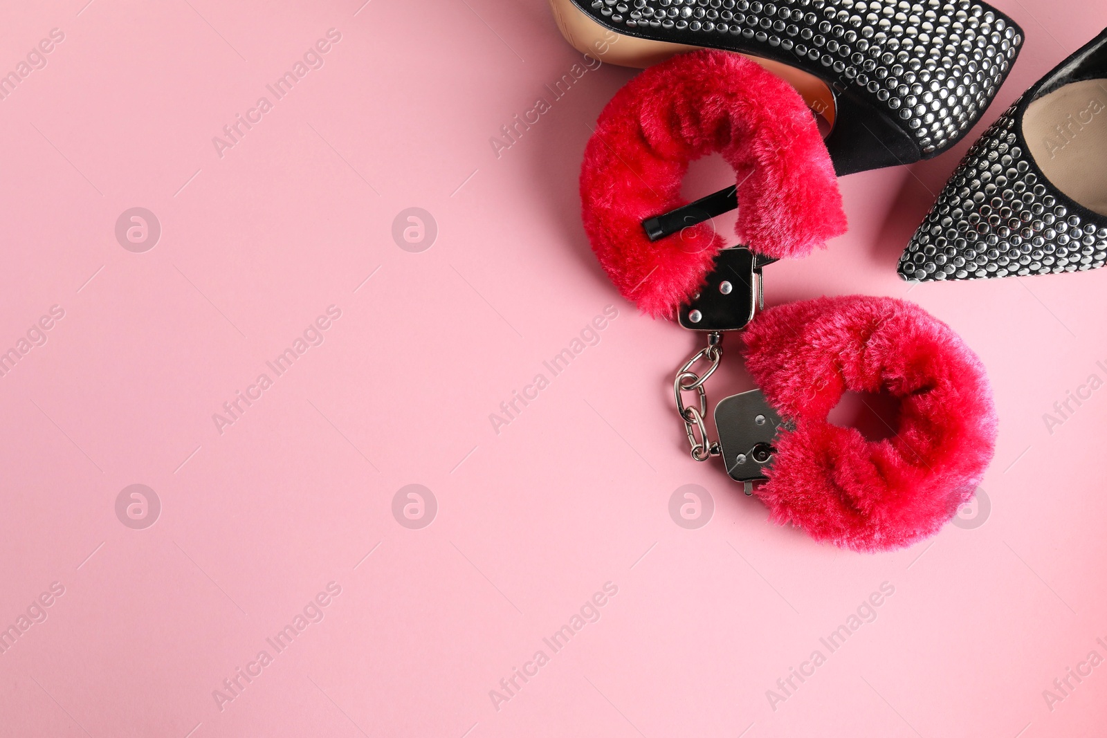 Photo of Fluffy handcuffs and high-heeled shoes on pink background, flat lay. Space for text