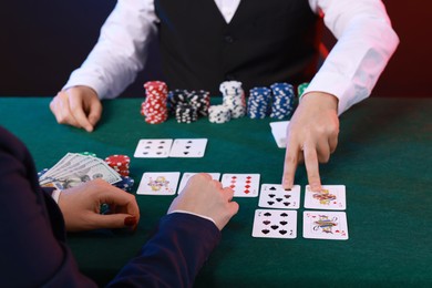 Photo of Professional croupier and gambler at table with playing cards and casino chips, closeup