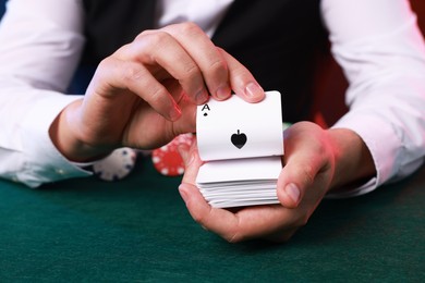 Photo of Professional croupier with playing cards at gambling table, closeup