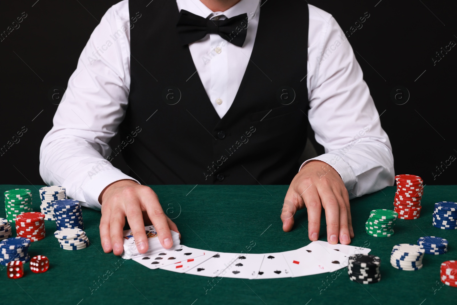 Photo of Professional croupier with playing cards at gambling table, closeup