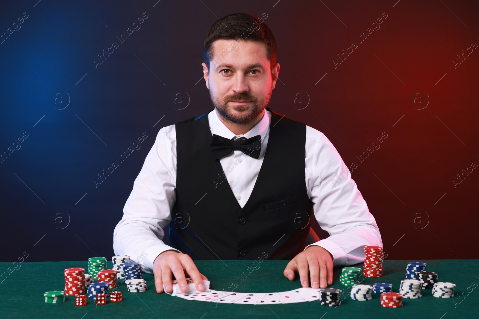 Photo of Professional croupier with playing cards at gambling table against color background