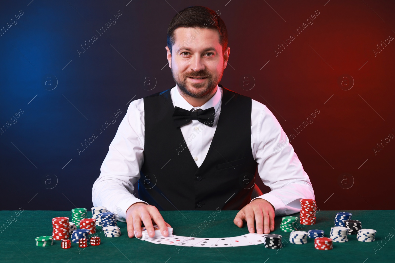 Photo of Professional croupier with playing cards at gambling table against color background