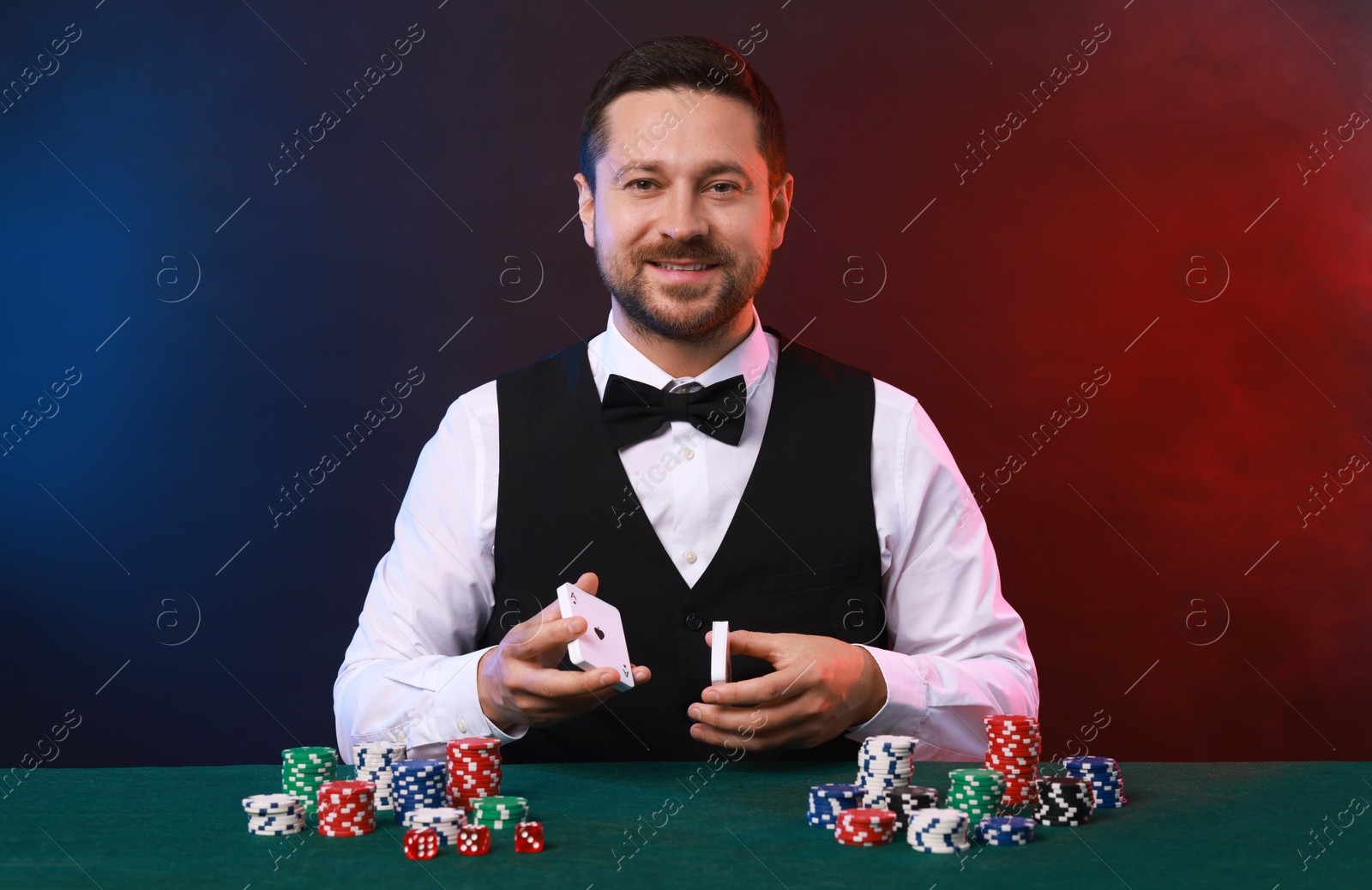 Photo of Professional croupier with playing cards at gambling table against color background