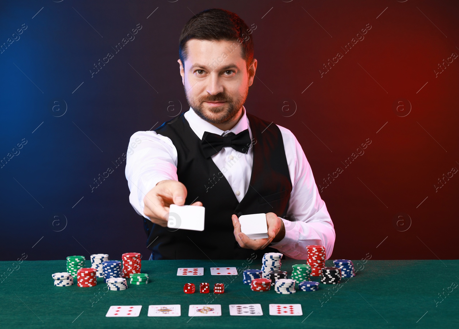 Photo of Professional croupier with playing cards at gambling table against color background