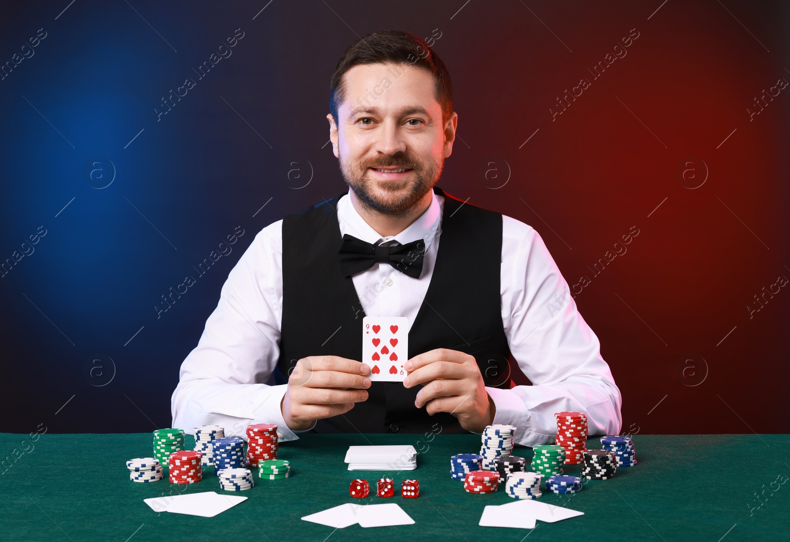 Photo of Professional croupier with playing card at gambling table against color background