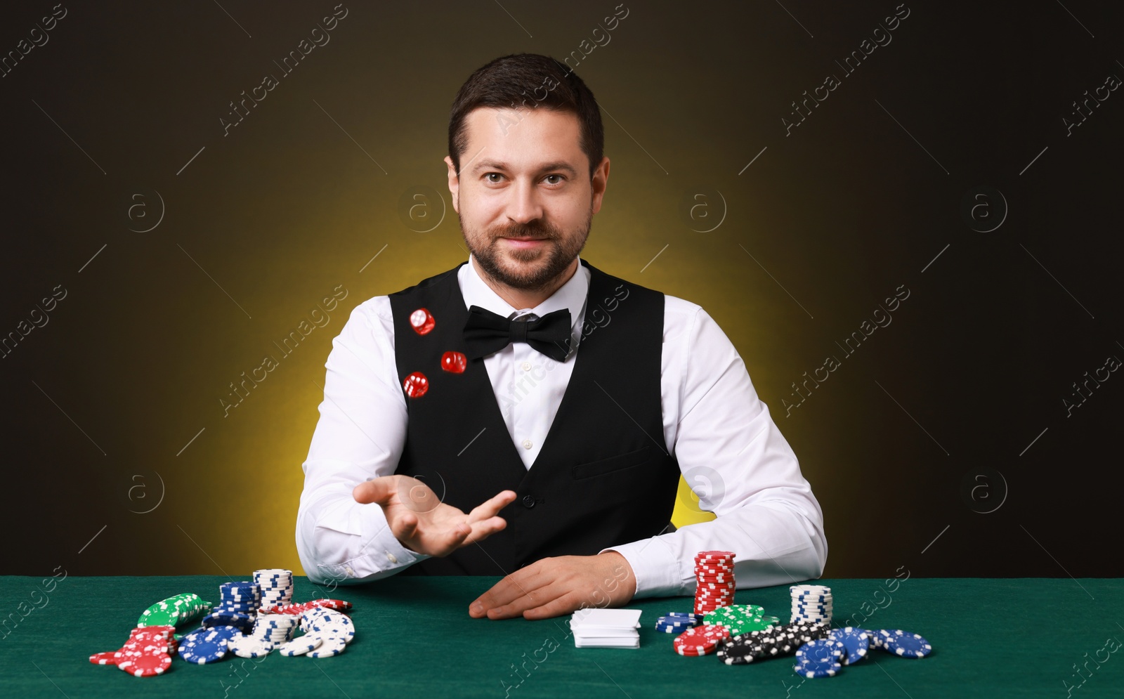 Photo of Professional croupier with dice at gambling table on dark yellow background