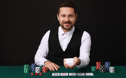 Photo of Professional croupier with playing cards at gambling table against black background