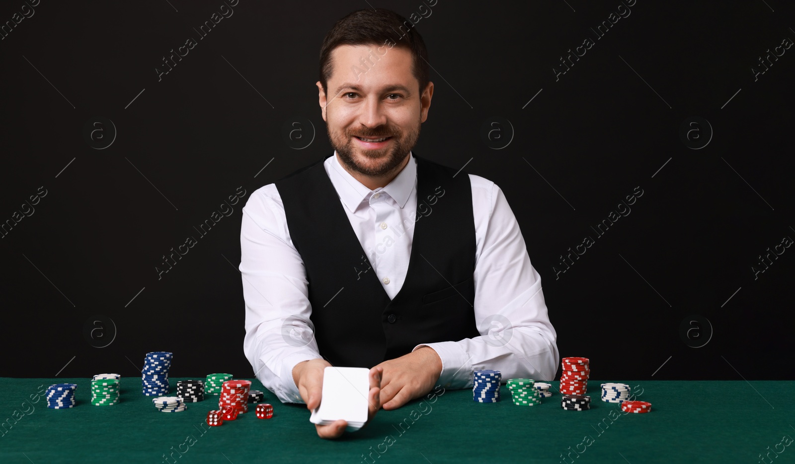 Photo of Professional croupier with playing cards at gambling table against black background