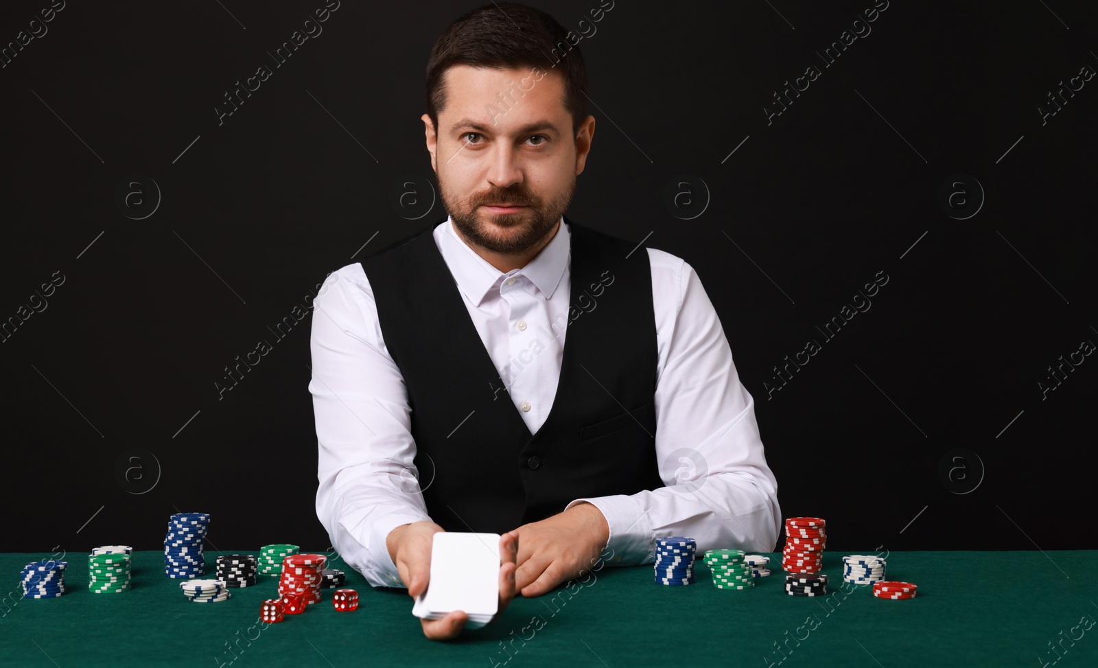 Photo of Professional croupier with playing cards at gambling table against black background