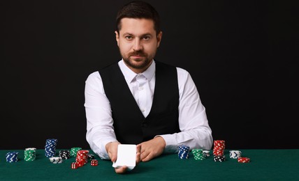 Photo of Professional croupier with playing cards at gambling table against black background