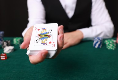 Photo of Professional croupier with playing cards at gambling table, closeup