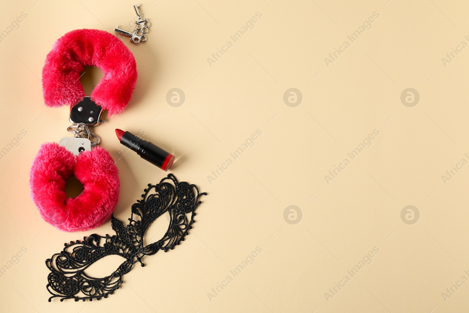 Photo of Pink fluffy handcuffs, lace mask, lipstick and keys on pale yellow background, flat lay. Space for text