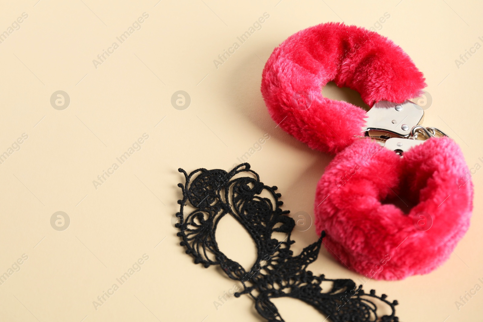 Photo of Pink fluffy handcuffs and lace mask on pale yellow background, flat lay. Space for text