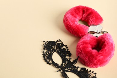 Photo of Pink fluffy handcuffs and lace mask on pale yellow background, flat lay. Space for text