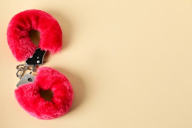 Photo of Pink fluffy handcuffs on pale yellow background, top view. Space for text