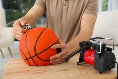 Photo of Man inflating basketball ball with air compressor indoors, closeup