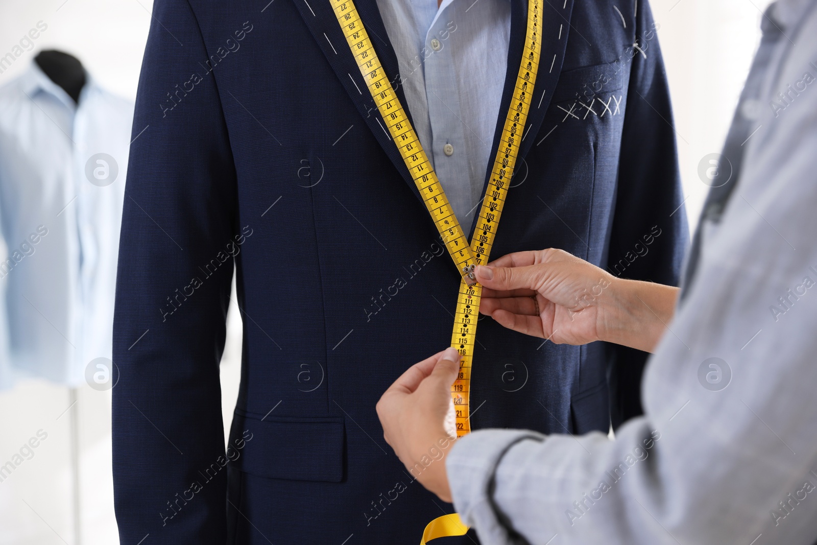 Photo of Tailor measuring jacket on man during fitting in atelier, closeup